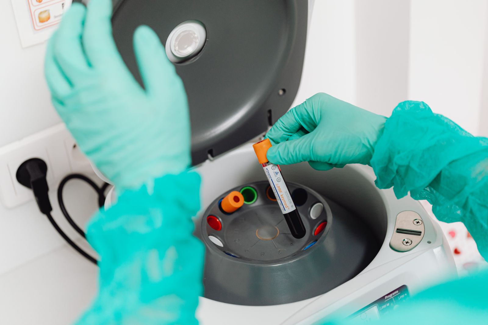 A laboratory technician loading a blood sample tube into a centrifuge.