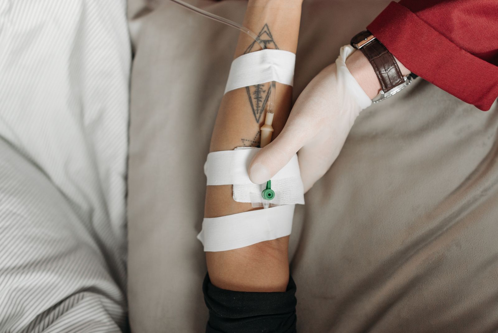 A gloved clinician securing an intravenous line in a patient's forearm.